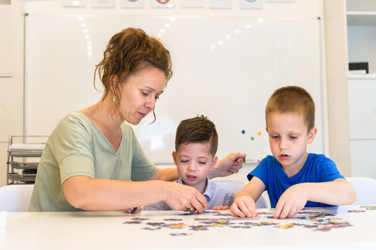 Teacher Woman And Two Preschooler Boy Playing With Puzzle Game In The Classroom