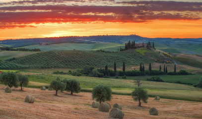 Magnificent spring landscape at sunrise.Beautiful view of typical tuscan farm house, green wave hills, cypresses trees, hay bales, olive trees, beautiful golden fields and meadows.Italy, Europe