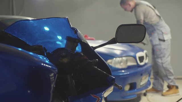 Sport bike on the foreground and master polishes the deep blue car