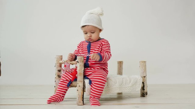 child sits on a small wooden bed in red striped pajamas