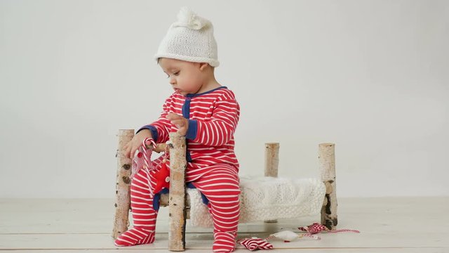 child sits on a small wooden bed in red striped pajamas