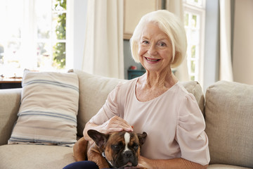 Senior Woman Sitting On Sofa At Home With Pet French Bulldog