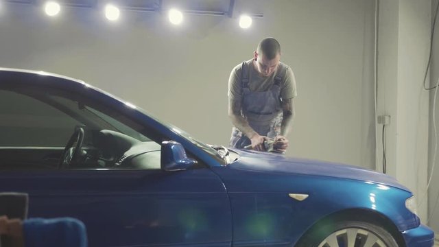 Master polishes the deep blue sport car via polish mashine in a car workshop