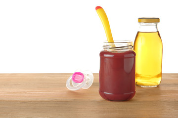 Jar with yummy baby food and bottle of juice on wooden table against white background