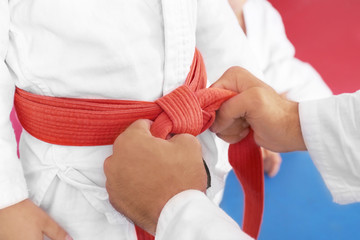 Karate instructor tying belt on child's waist, closeup