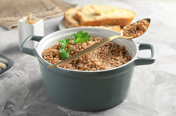 Casserole and spoon with tasty buckwheat porridge on table