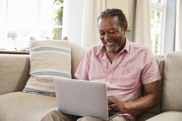 Senior Man Sitting On Sofa Using Laptop At Home Together - Powered by Adobe