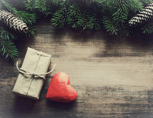 Red heart and Christmas gift on a wooden old surface in an environment of fir-tree branches, top...