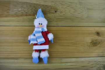 Christmas photography image with hand made knitted happy white snowman in blue hat scarf red coat and boots on natural wood background