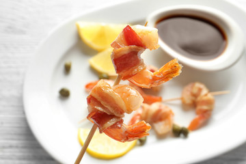 Bacon-wrapped shrimps on skewer over plate, closeup