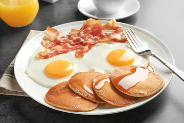 Tasty breakfast with pancakes, fried eggs and bacon on table