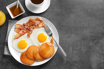 Tasty breakfast with pancakes, fried eggs and bacon on grey background