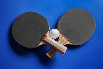 Two ping pong rackets and ball on blue background