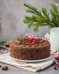 Traditional Christmas English pudding (fruit cake) with rosemary and cranberries on white plate on a concrete light background. Christmas decor of the table.  