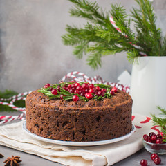 Traditional Christmas English pudding (fruit cake) with rosemary and cranberries on white plate on a concrete light background. Christmas decor of the table.  