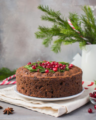 Traditional Christmas English pudding (fruit cake) with rosemary and cranberries on white plate on...