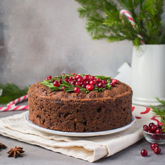 Traditional Christmas English pudding (fruit cake) with rosemary and cranberries on white plate on a concrete light background. Christmas decor of the table.  