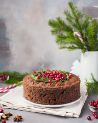 Traditional Christmas English pudding (fruit cake) with rosemary and cranberries on white plate on a concrete light background. Christmas decor of the table.  