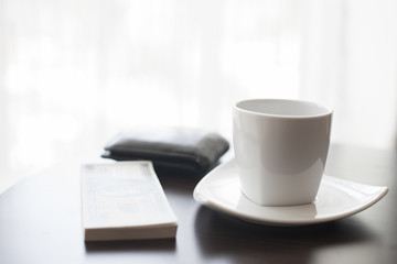 Cup of black coffee, newspaper and a pen against the window in the morning