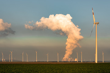 Wind farm and power plant, producing clouds of steam at dusk. Combination of renewable energy...