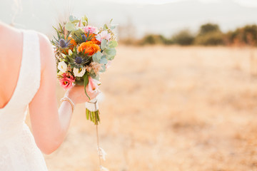 The bride is holding wedding bouquet from orange, whire, pink flowers and standing on background of...