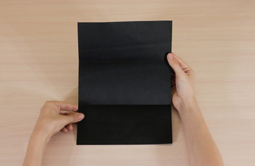 Obraz premium Hands holding blank black brochure booklet in the hand. Leaflet presentation. Pamphlet hand man. Show offset paper. Sheet template. Book in hands. Booklet folding design. Fold paper sheet.