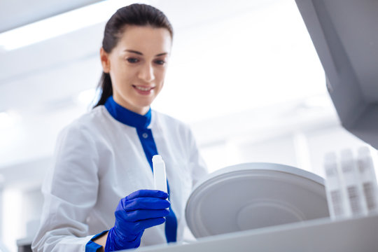 Start working. Selective focus of white medical container hold by brunette  enthuasiastic female laboratory assistant who wearing labcoat and smiling