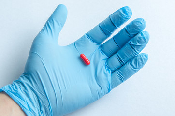 The hand of the medical worker in medical gloves holding a pill