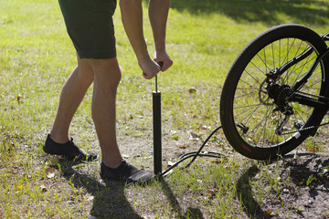 Obraz premium Inflating the tire of a bicycle. Cyclist repairs bike in forest. Bicyclist pumping air into the wheel. Biker uses a bicycle pump. Pumping air into an empty wheel of bike.