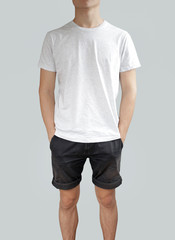 Obraz premium White t shirt and black shorts on a young man template on grey background. Hands in pockets.