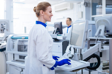 Data base. Attractive smart pleasant male scientist searching for additional information in the computer while putting his hand near the monitor  and posing in the laboratory