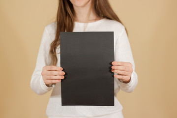 Girl holding black A4 blank paper vertically. Leaflet presentation. Pamphlet hold hands. Woman show...