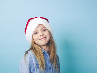 young beautiful blond girl with christmas hat in front of blue backgroubd