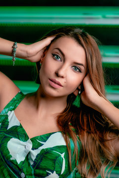 Portrait of stylish brown hair woman in green dress, green earrings, with makeup on green background in photostudio