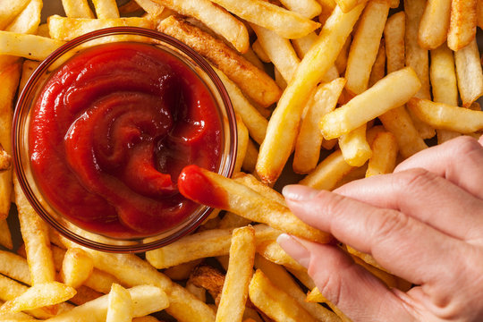 Hand dipping french fries in tomato sauce or ketchup