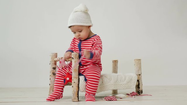 child sits on a small wooden bed in red striped pajamas