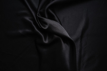 Dark black silky, satin  fabric, wave, draperies. Beautiful textile backdrop. Close-up. Top view 