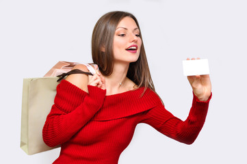 Beautiful woman in red dress holding white card in her hand and the shopping bags behind her