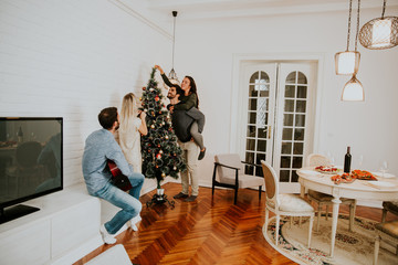 Fototapeta premium Young people decorate fir-tree for holidays of Christmas and New Year at home