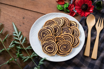 Spiral Cookies with a white cup of coffee and red flower on a wooden table. Handmade biscuits