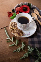 Fototapeta na wymiar Spiral Cookies with a white cup of coffee and red flower on a wooden table. Handmade biscuits
