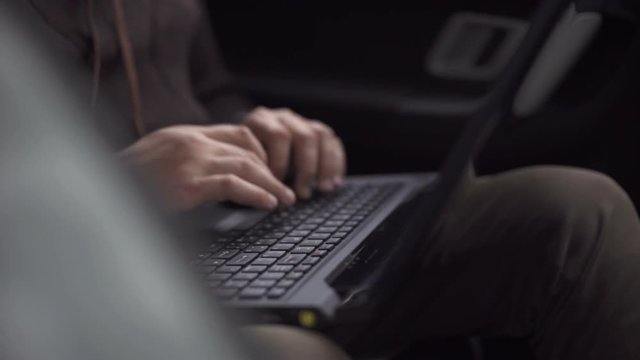 A man is working in a car typing text on a laptop