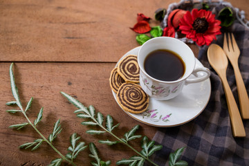 Spiral Cookies with a white cup of coffee and red flower on a wooden table. Handmade biscuits