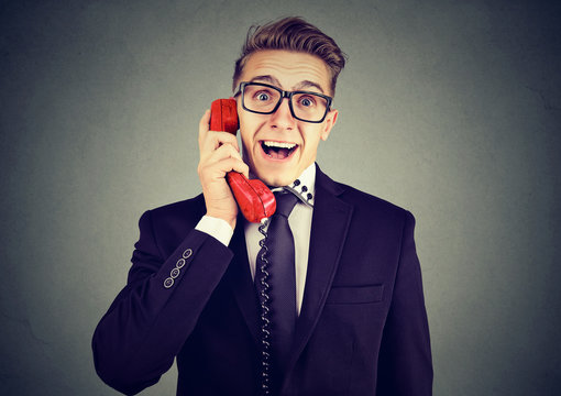 Happy business man receiving good news winning on the phone isolated on gray wall background 