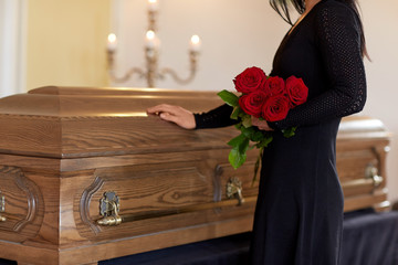 sad woman with red roses and coffin at funeral
