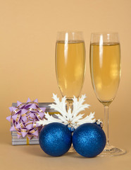 Wine glasses with sparkling champagne, gift, Christmas toys on beige