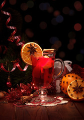 Spicy warming winter drink in glass, fruit and spices, New Year's tinsel, isolated on black