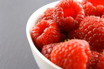 fresh red raspberry fruits in a small white bowl