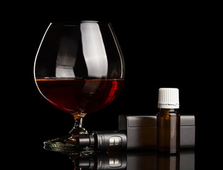 Glass with brandy, electronic cigarette and liquid for smoking isolated on black
