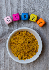 Curry in Schale mit Buchstabenwürfel auf Holzuntergrund